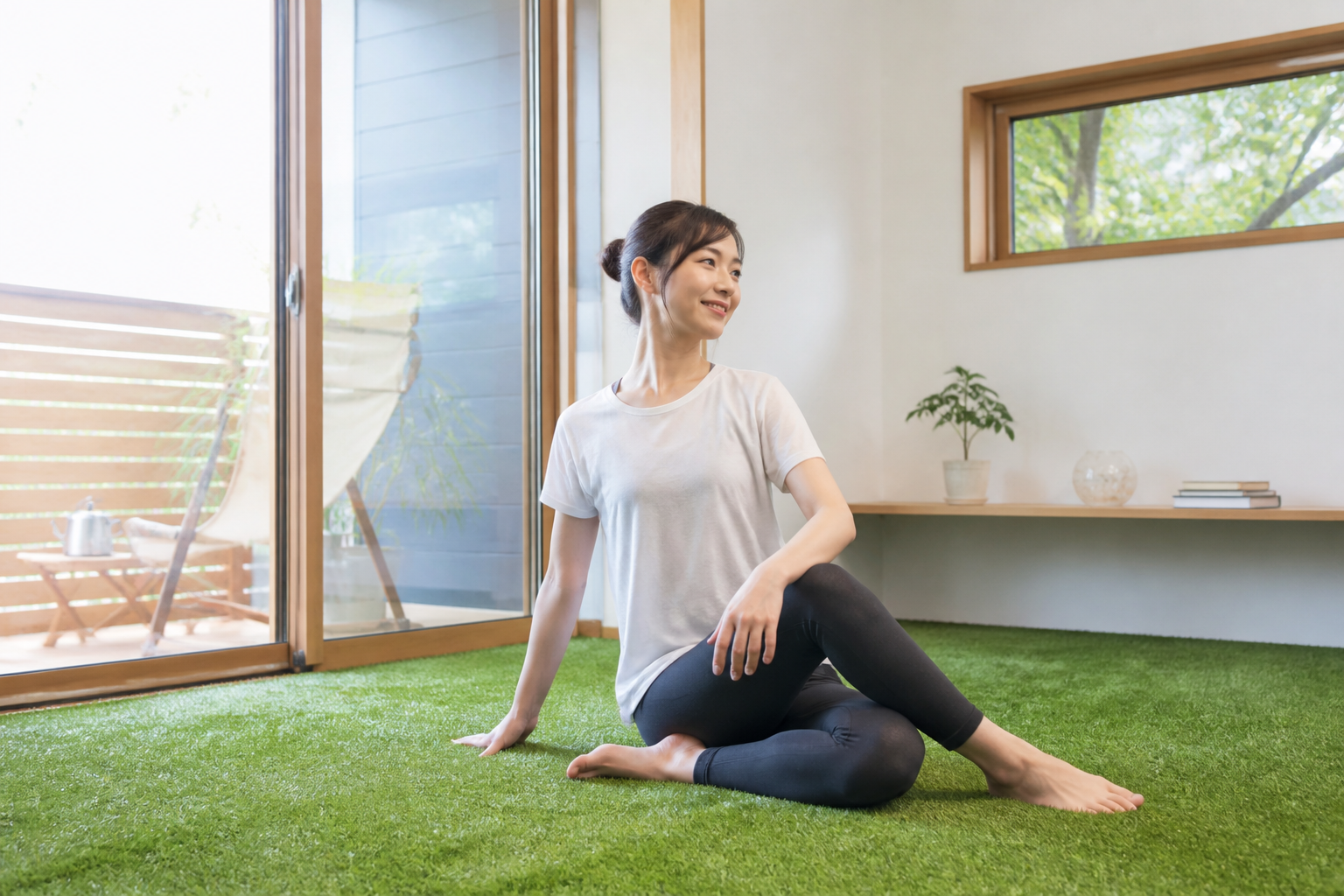 室内の人工芝の上で、女性がヨガやストレッチをしている様子の写真。快適さが伝わるもの。]